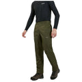 A person is wearing waterproof olive-green pants and a black long-sleeve shirt while standing on a flat surface, suggestive of outdoor or hiking attire with rugged boots.